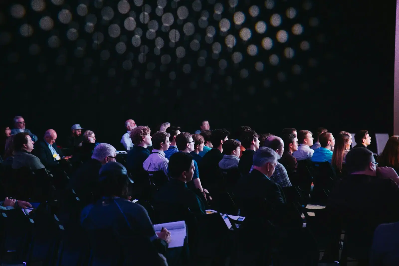 An audience seated in rows in a dark hall, lit from the stage