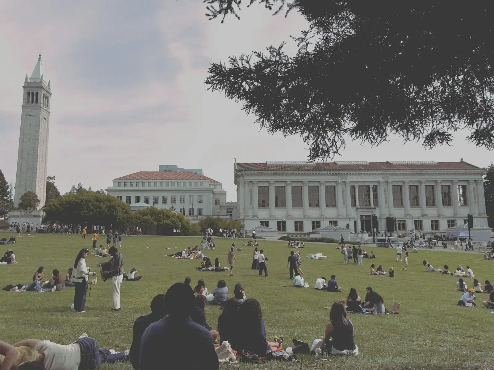 Students sitting and walking on a wide campus lawn below a clock tower and a columned library