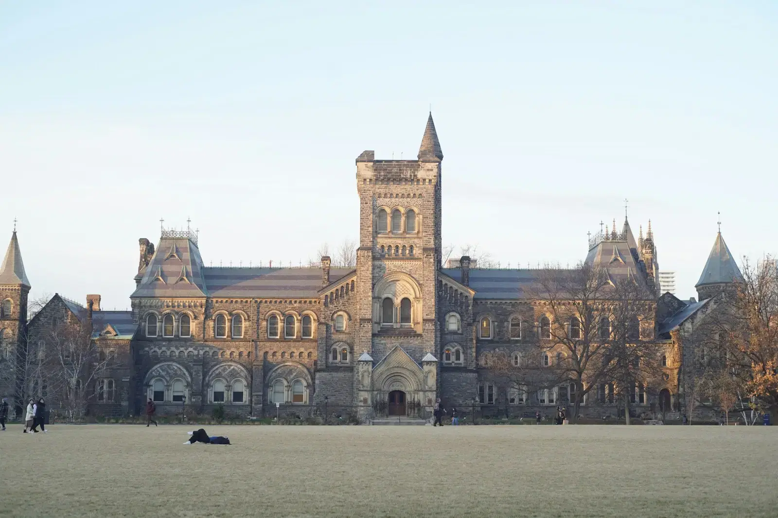A stone college building with a central tower across an open lawn in late light