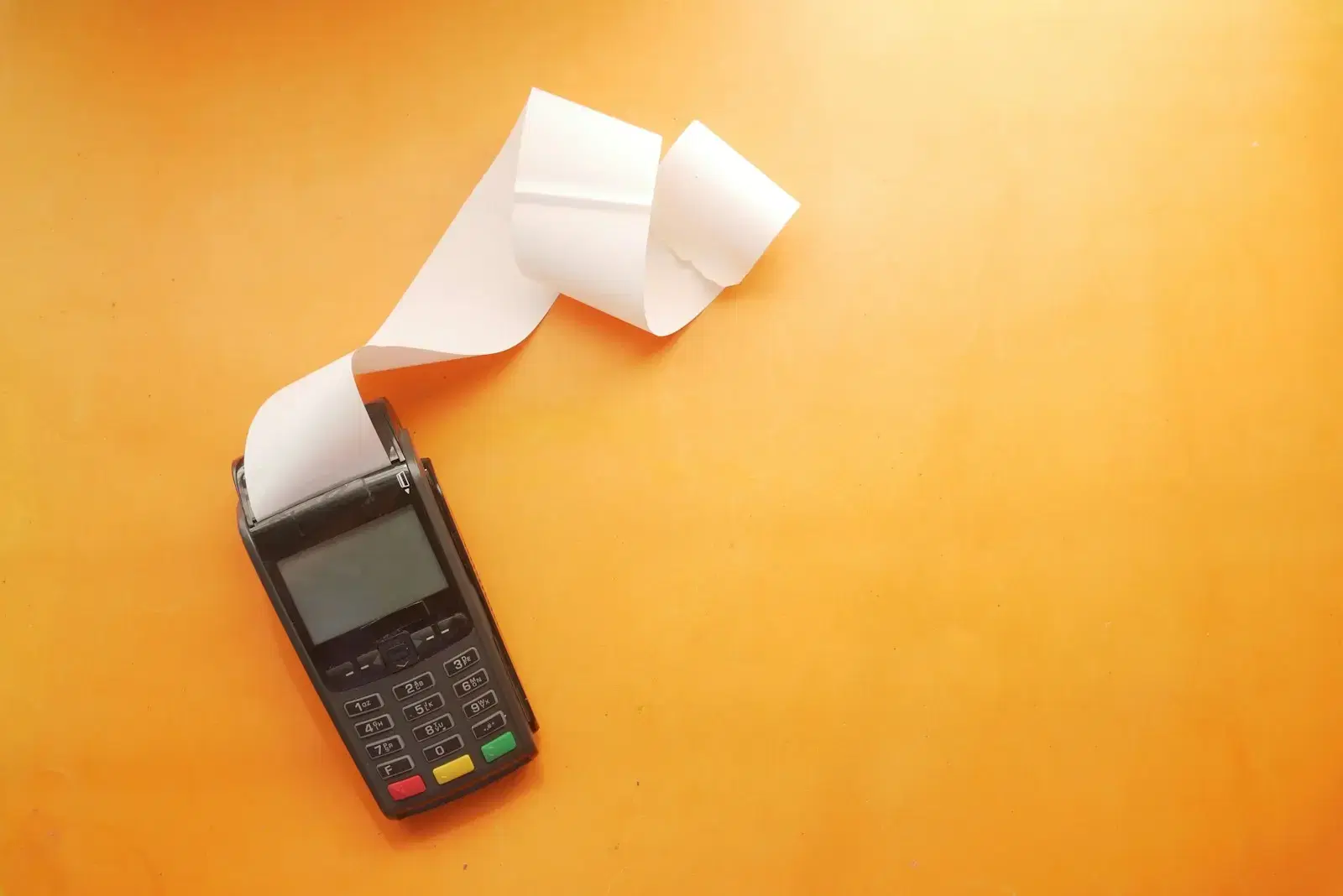 A card terminal printing a long receipt on an orange surface