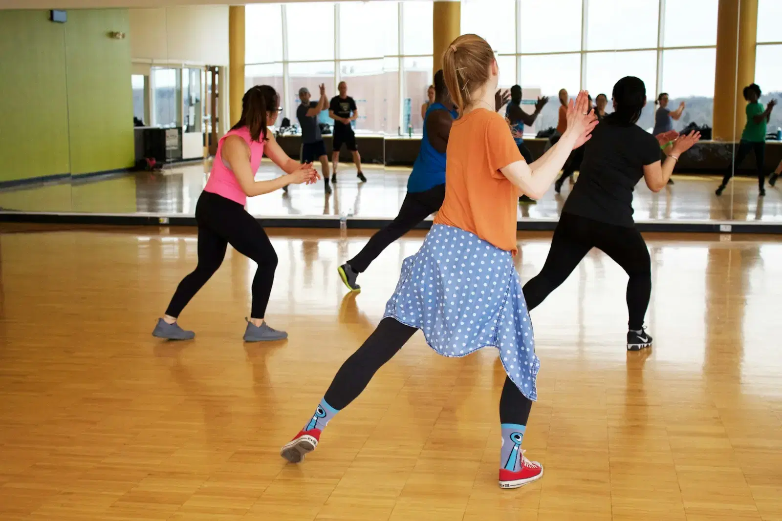 A dance class mid-move on a wooden floor in front of a mirror wall