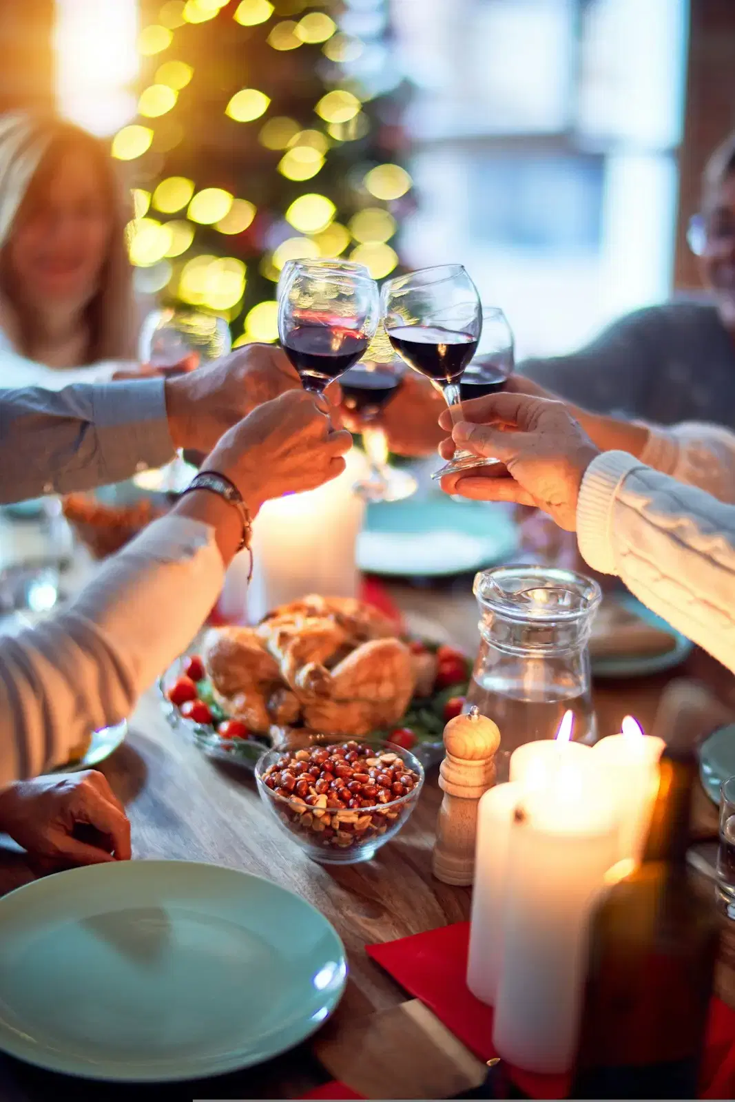 Hands raising glasses of red wine over a candlelit holiday table, the faces out of focus