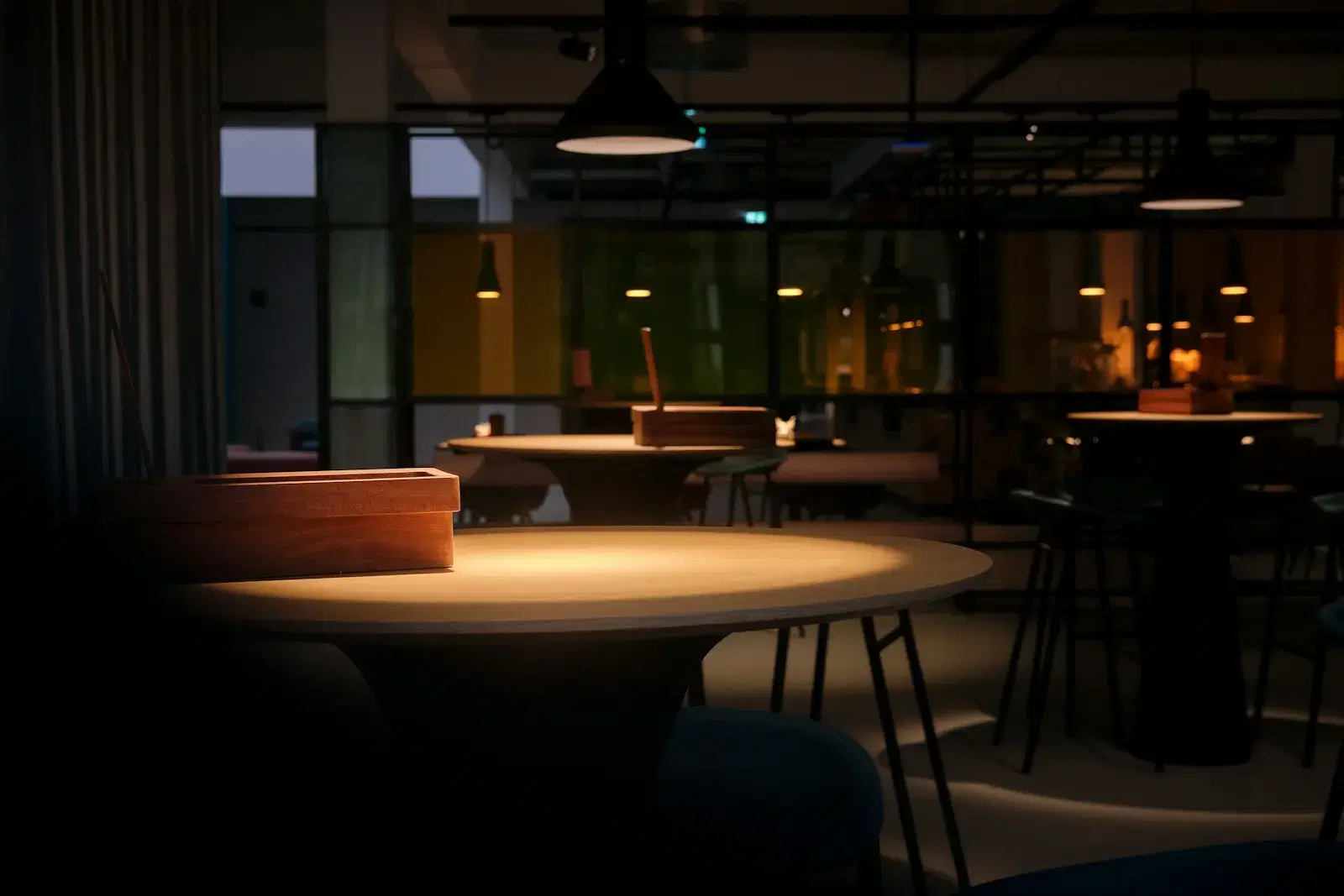 An empty restaurant at night, a pool of lamplight on a round table, the rest of the room in shadow