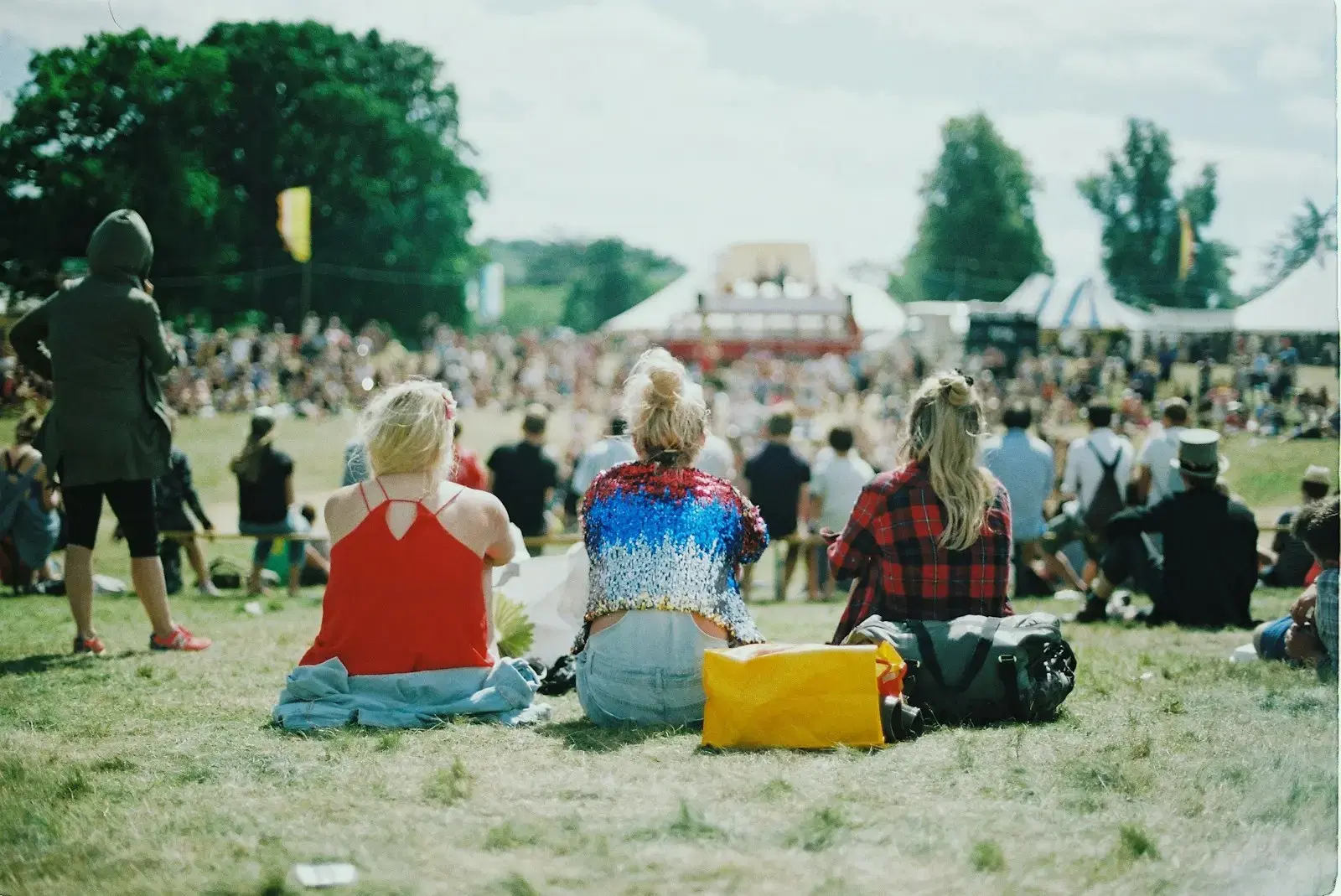 A crowd sitting and standing on a festival lawn on a sunny day