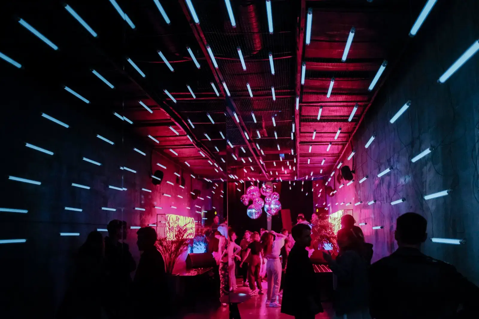 People standing in a long dark room lit pink, under rows of blue light bars