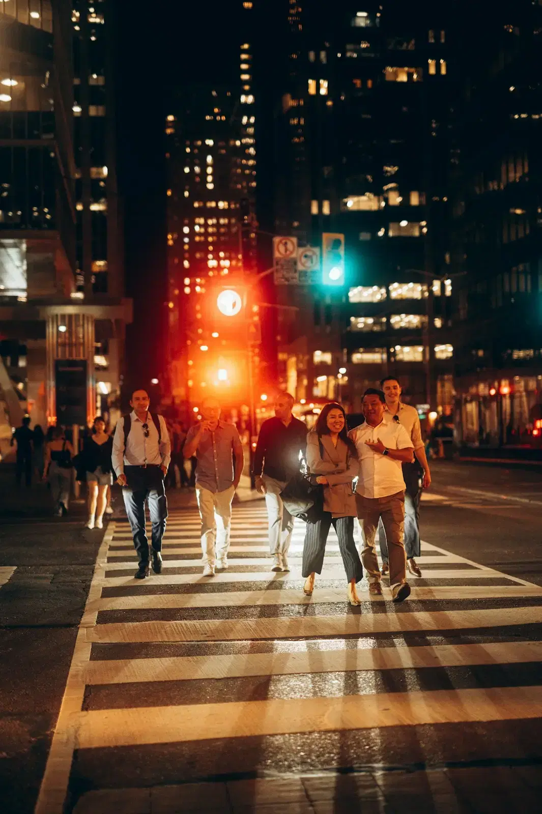 Friends crossing a wide street at night, lit by traffic lights and headlights