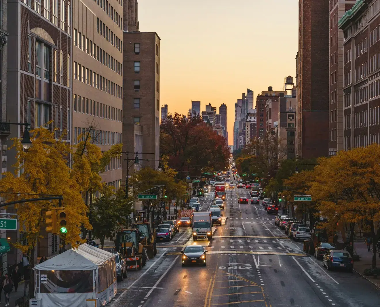 An avenue in Manhattan at dusk, lined with autumn trees, midtown towers in the distance