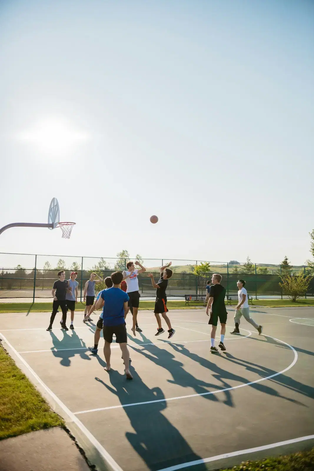 A pickup game on an outdoor court, the ball in the air and long shadows on the asphalt