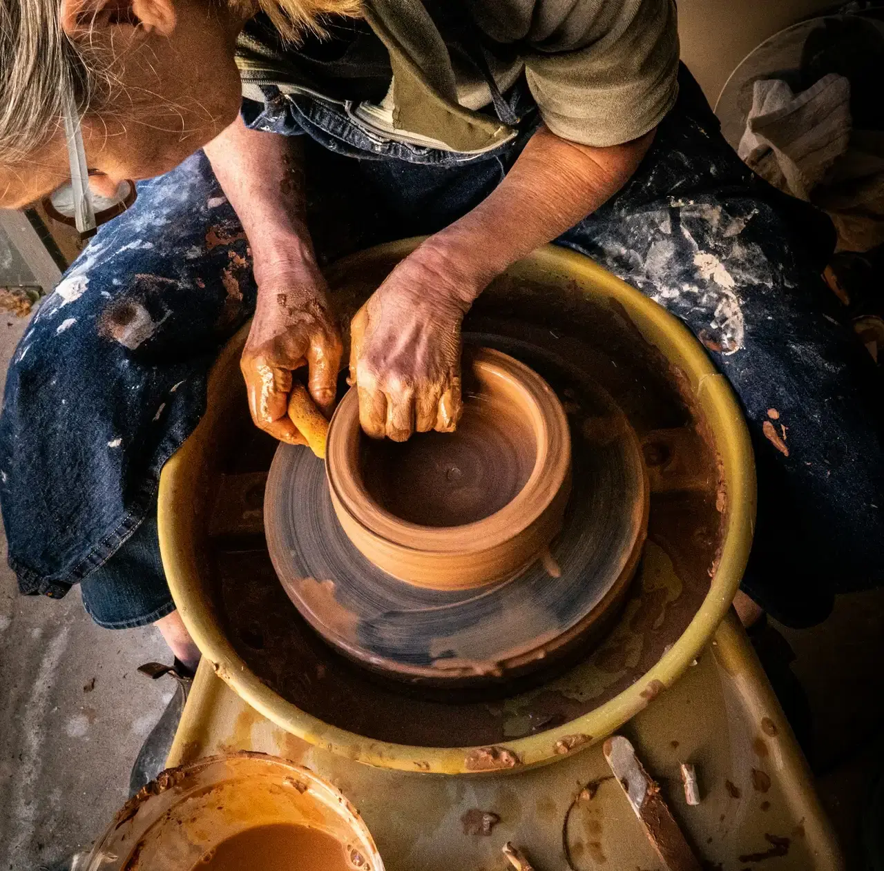Clay-covered hands shaping a bowl on a spinning pottery wheel